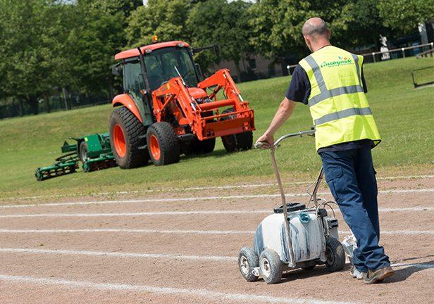 Man with Countrywide hi-viz vest painting a white line on a sports running track