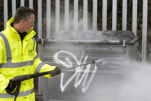 man removing graffiti removal off a bin with a jet wash